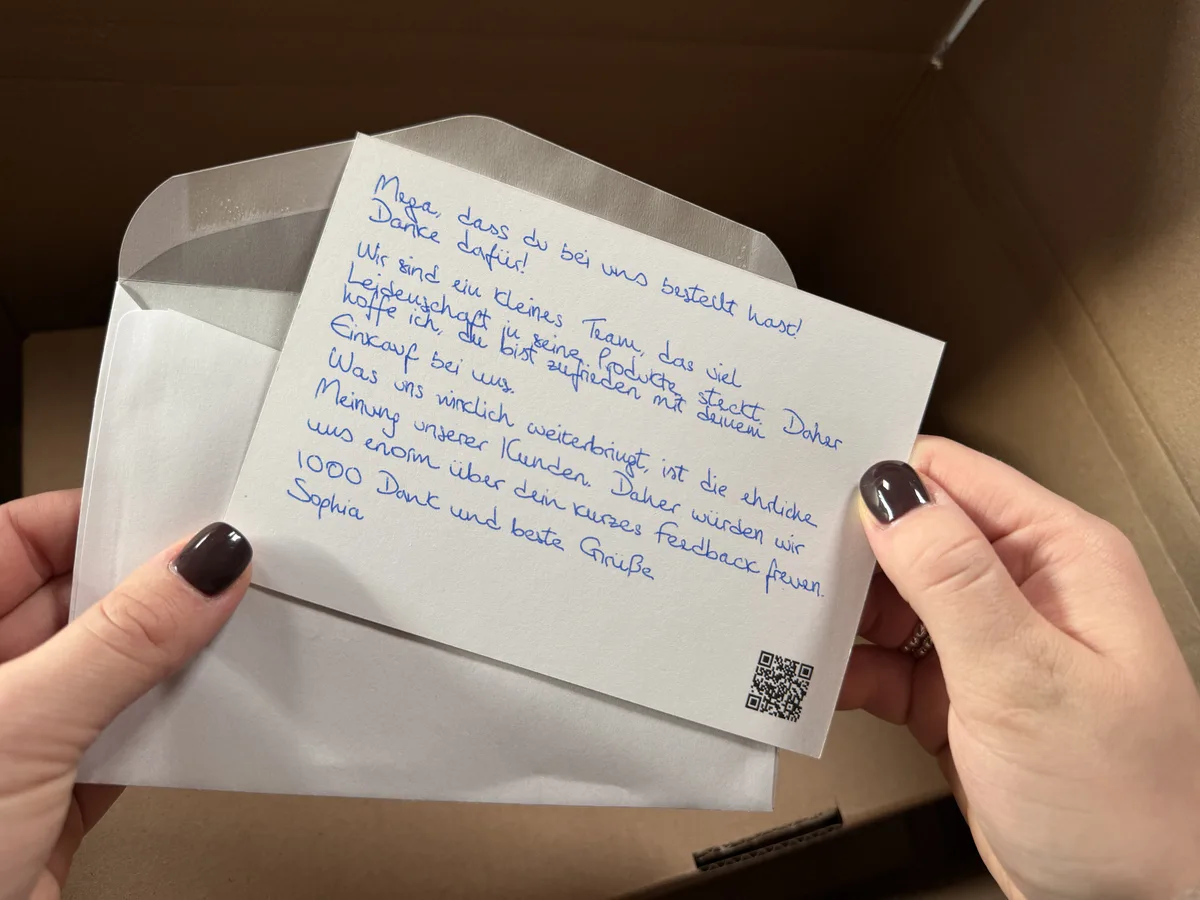 Hände halten eine handgeschriebene Karte mit QR-Code über dem Paket